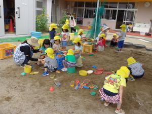 園児たちが先生と一緒に砂場で遊んでいる写真
