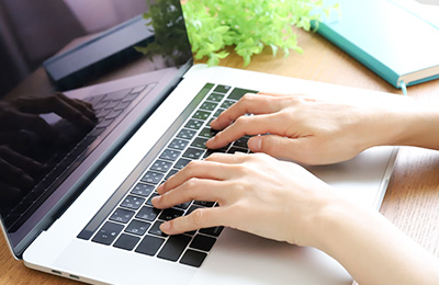 ノートパソコンにタイピングしている様子の写真