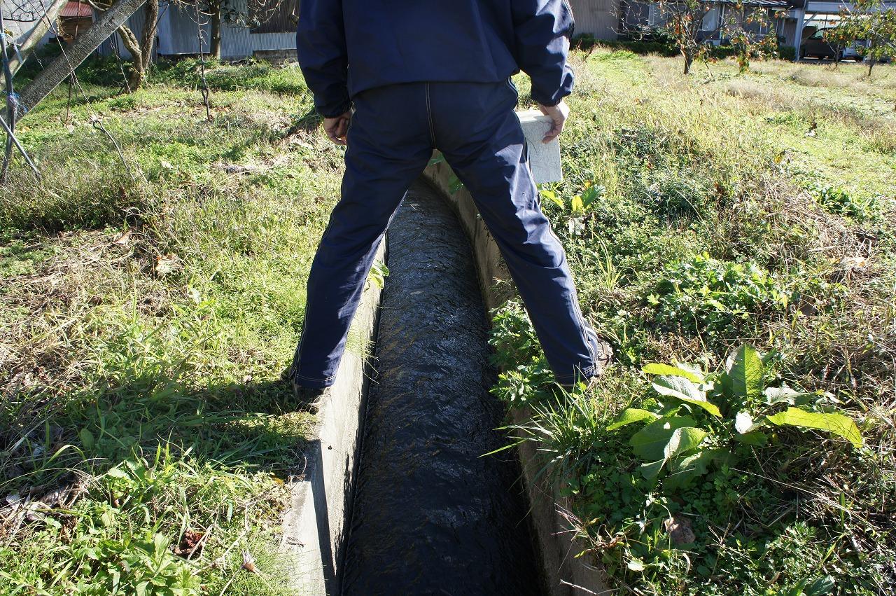 水路幅をまたいでいる男性の後ろ姿の写真