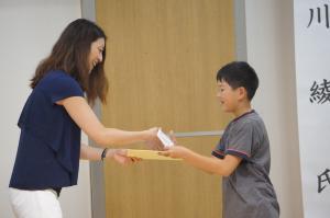 抽選会で当選した人に商品を渡す寺川さんと受け取る児童の写真